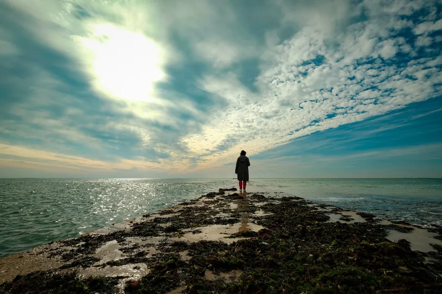 A person walking out along a spit of land into the sea
